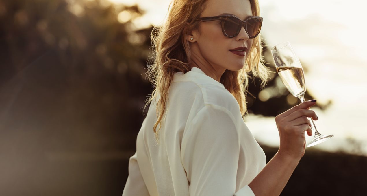 Frau in weißem Outfit mit Sonnenbrille und Champagnerglas – stilvolle Begleitung in Köln